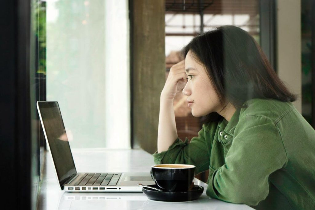Woman sitting in a coffee shop with a laptop and coffee, looking thoughtful